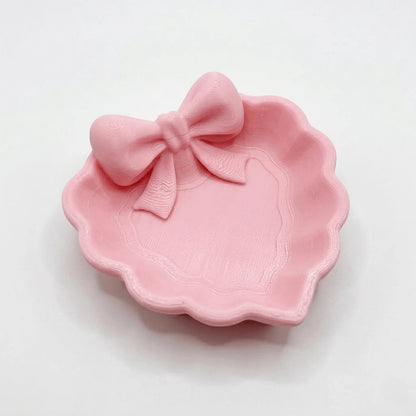 A heart-shaped jewelry tray with a pink bow, made using 3D printing technology, is suitable for placement on a dressing table, s