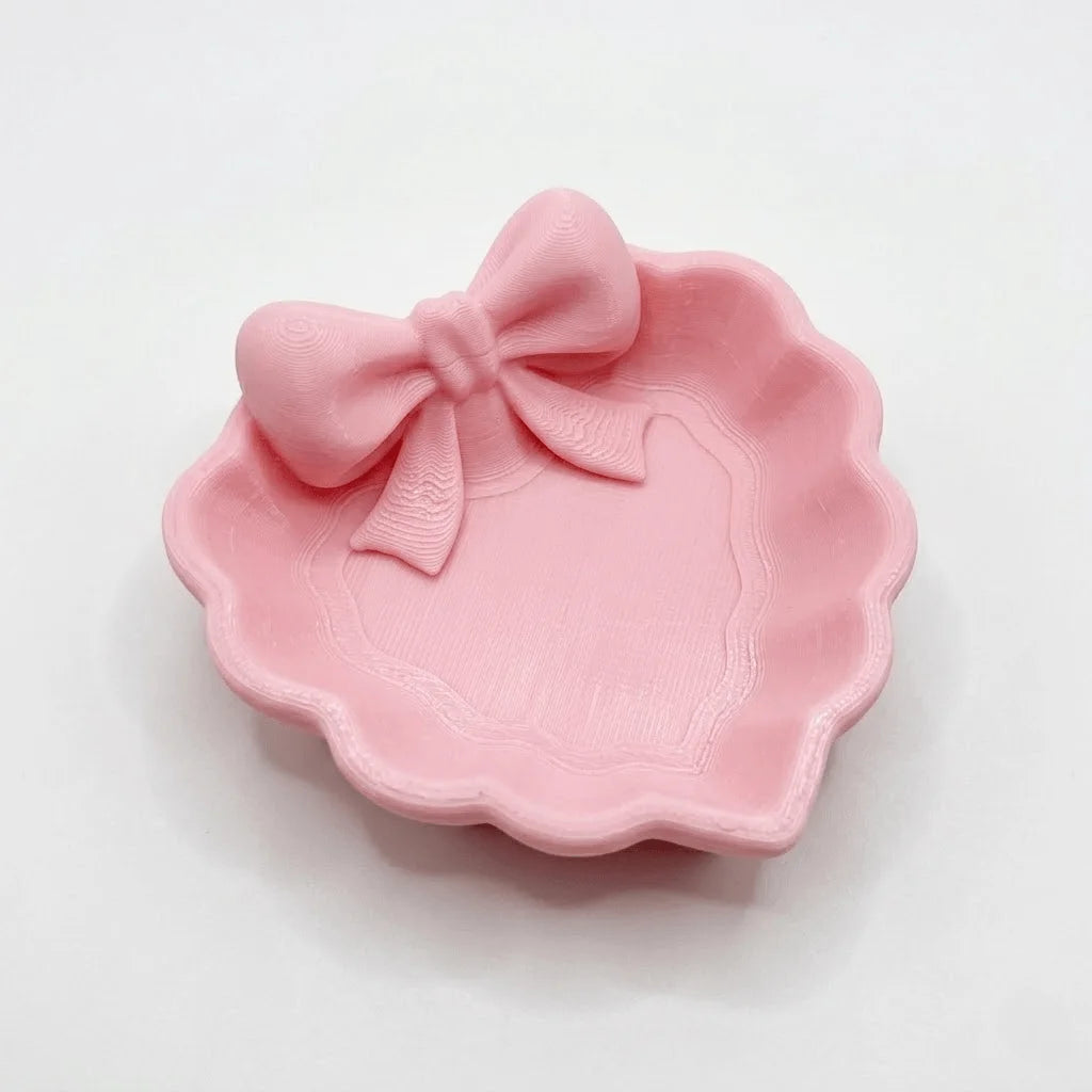 A heart-shaped jewelry tray with a pink bow, made using 3D printing technology, is suitable for placement on a dressing table, s