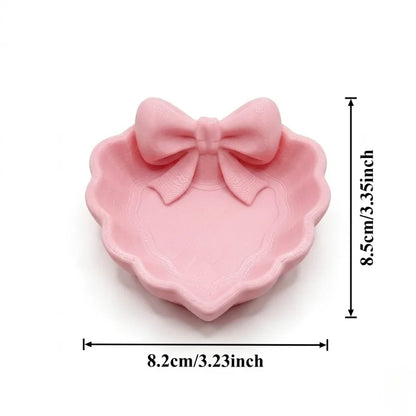 A heart-shaped jewelry tray with a pink bow, made using 3D printing technology, is suitable for placement on a dressing table, s