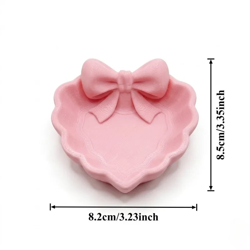 A heart-shaped jewelry tray with a pink bow, made using 3D printing technology, is suitable for placement on a dressing table, s