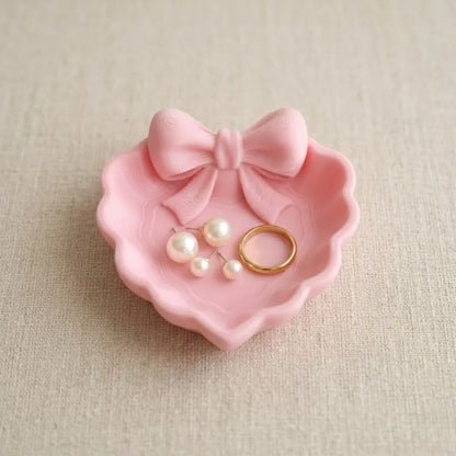A heart-shaped jewelry tray with a pink bow, made using 3D printing technology, is suitable for placement on a dressing table, s